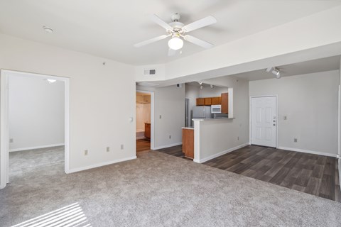 an empty living room with a ceiling fan and a kitchen